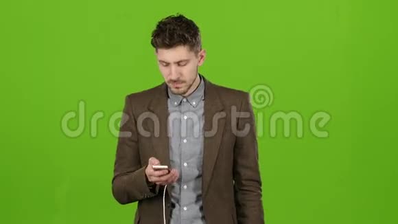 商人拿着手机和耳机选择音乐听绿色屏幕视频的预览图