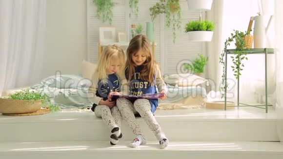 两个小女孩在一个有植物的明亮房间里看书视频的预览图
