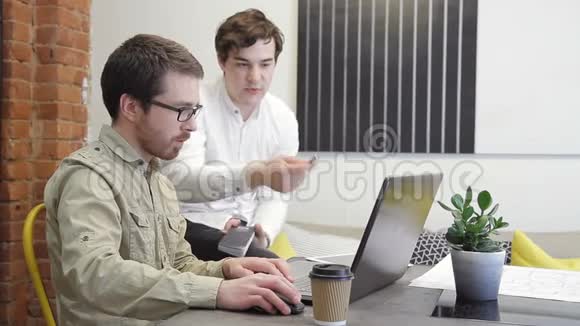 两位同事在办公室的笔记本电脑中使用互联网查看信息视频的预览图