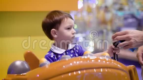 小男孩骑在明亮的圆形旋转木马附近的游乐园里的大玩具车上拿着真正的汽车钥匙视频的预览图