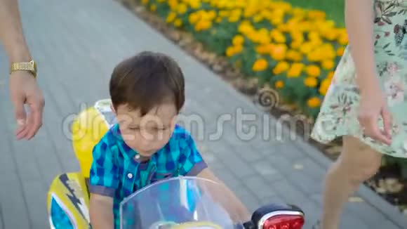 夏天一个黑发男孩正骑着玩具摩托车在公园里靠近他的父母视频的预览图