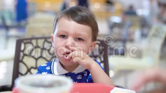 小黑头发的男孩正坐在椅子上在餐馆里吃着带酱汁的炸薯条视频的预览图