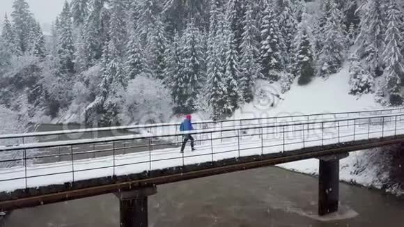 在雪山针叶林和女孩的暴风雪中飞行在桥上走过靠近山河的一条小路视频的预览图
