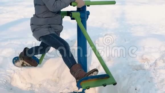 特写镜头中的女人腿在城市冬季公园的模拟器上做腿部运动侧视图视频的预览图