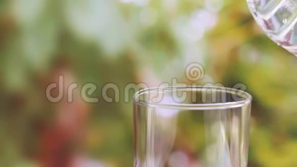 女人手拿水瓶在模糊的绿色自然背景上向玻璃中倒入清澈的饮用水视频的预览图