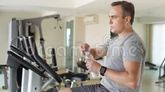 有决心的英俊身材的年轻人在健身房做运动骑自行车从塑料瓶里喝水视频的预览图