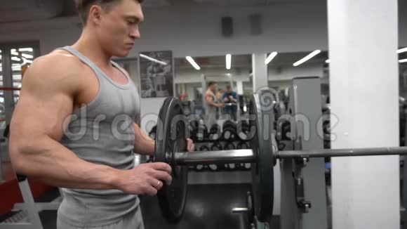 决心肌肉发达的男人把沉重的盘子放在杠铃上并在健身房里举起视频的预览图
