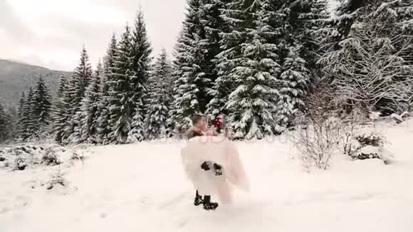 新郎在雪地里旋转着快乐的新娘手里握着她在雪地里旋转着冷杉林视频的预览图