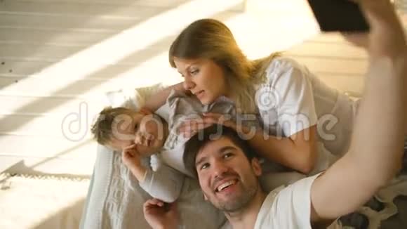 微笑的父母带着孩子在家里的床上自拍全家福视频的预览图