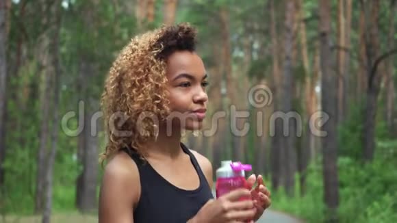 黑色女人从粉红色的瓶子里喝黑人年轻女子慢跑后休息的肖像视频的预览图