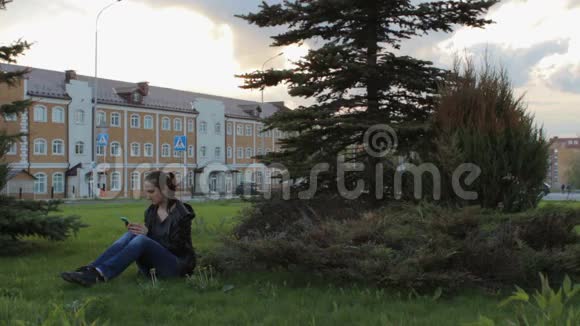 坐在城市公园草地上的年轻女子使用智能手机视频的预览图