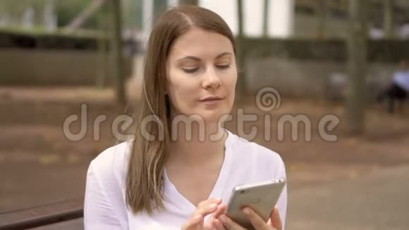 穿着白色衬衫坐在公园里的女商人的肖像使用手机的专业女性视频的预览图