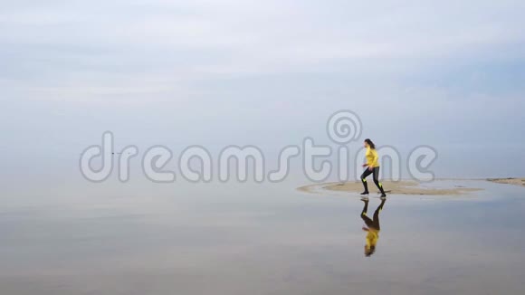 年轻的慢跑女子身材苗条日出时在海滩上奔跑慢动作视频的预览图