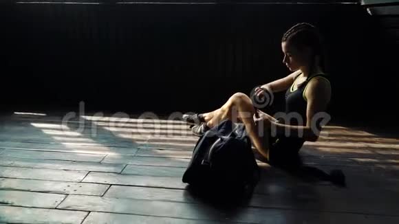 惊慌失措的年轻美女坐在地板上用黑色拳击包裹在俱乐部里的手视频的预览图