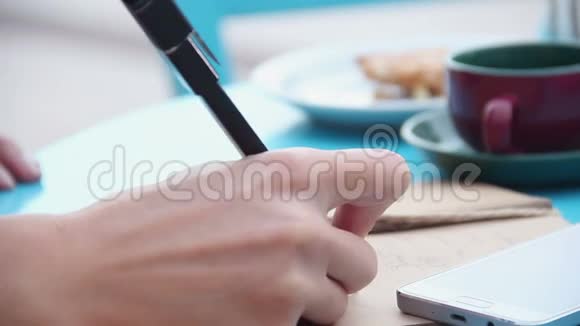 女人的手在笔记本上写字咖啡杯咖啡桌上的智能手机视频的预览图