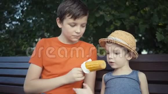 两个兄弟坐在公园的长凳上吃煮玉米视频的预览图