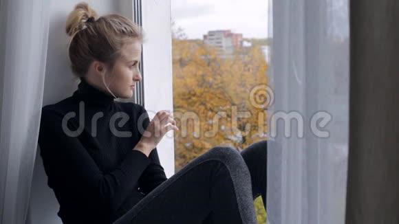 伤心的年轻女子坐在窗台上看着窗户视频的预览图