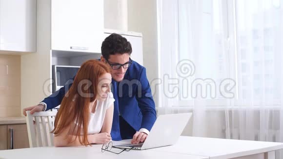 年轻的商务夫妇在家里的厨房里聊天和使用平板电脑视频的预览图