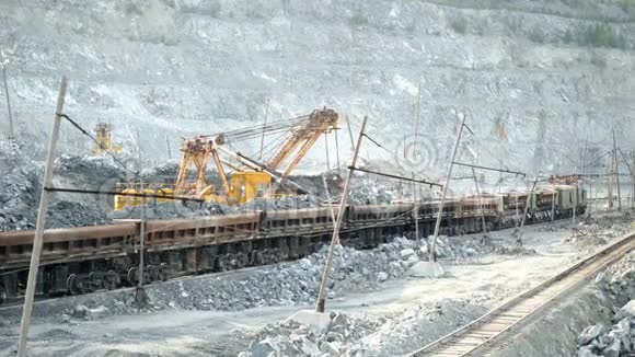 挖掘机和铁路用矿石挖掘机在露天矿背景下充满矿石轨道车采矿重型运输视频的预览图