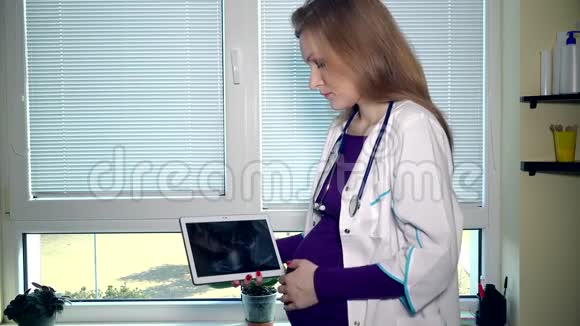 孕妇爱抚腹部并在平板电脑中查看超声波照片视频的预览图