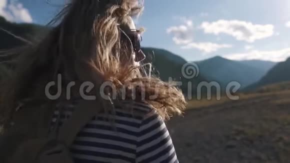 一个旅游女孩特写的肖像一个背着背包戴着太阳镜的旅行者穿过山区视频的预览图