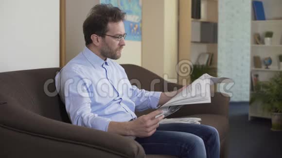 早晨的仪式放松的男人坐在沙发上在家看报纸视频的预览图