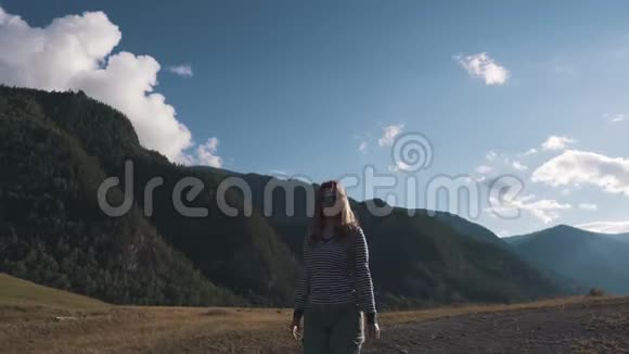 一个旅游女孩特写的肖像一个背着背包戴着太阳镜的旅行者穿过山区视频的预览图