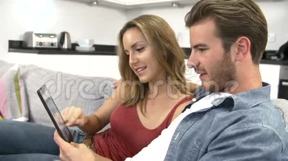 使用数码平板电脑坐沙发的年轻夫妇视频的预览图