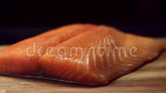 将新鲜美味的三文鱼牛排放在木切割板上隔离在黑色背景上生的红鱼片视频的预览图