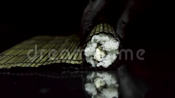 用黑竹轧工艺在黑色背景上隔离双手戴着黑色手套手拿寿司视频的预览图