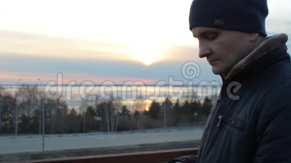 年轻人用智能手机户外站在屋顶桥上日落城景视频的预览图