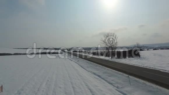 在冬天下雪的田野里很少有汽车在路上行驶阳光和雪空中射击视频的预览图