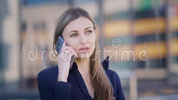 漂亮的长发商务女性正站在办公楼附近的街道上打电话女性视频的预览图