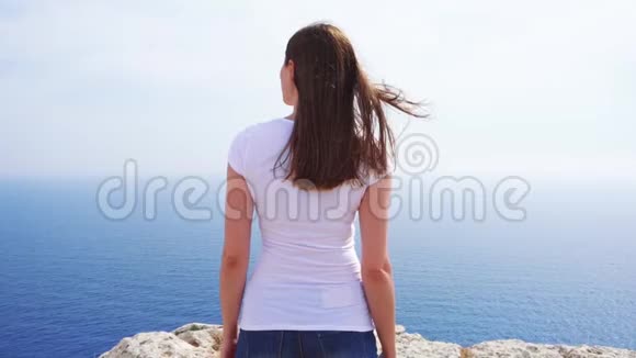 在阳光明媚的日子里女人缓慢地站在悬崖边免费女性看蓝色海景视频的预览图
