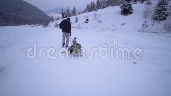 年轻的幸福家庭在雪林里玩得很开心父亲把他的小儿子卷在雪橇上晚上散步爸爸和爸爸视频的预览图