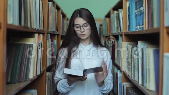 年轻漂亮的女孩穿着白色衬衫和眼镜在大学图书馆挑选书籍阅读视频的预览图
