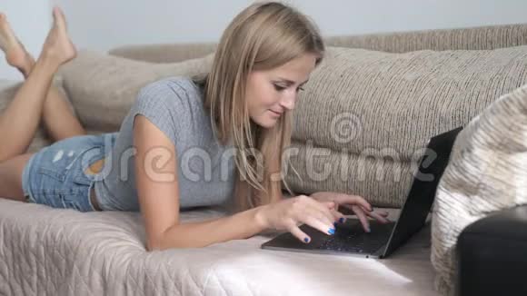 美丽的女人躺在家里的沙发上用她的笔记本电脑工作视频的预览图