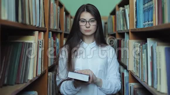 年轻漂亮的女孩穿着白色衬衫和眼镜在大学图书馆挑选书籍阅读视频的预览图