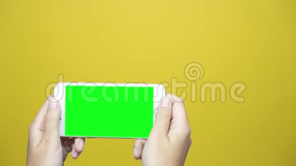 女士使用智能手机黄色桌子背景上有绿色屏幕女性手滚动网页轻敲触摸屏视频的预览图