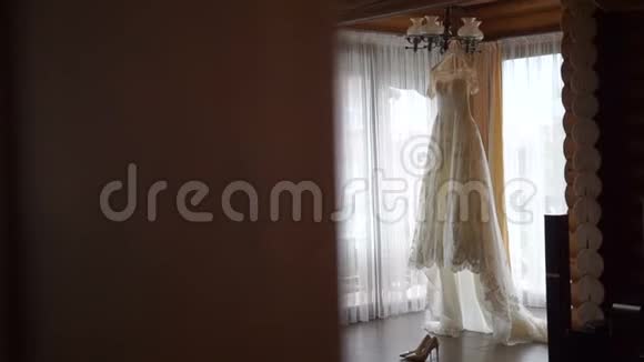 完美的白色婚纱挂在新娘房间的衣架上优雅的高跟鞋躺在长袍附近视频的预览图