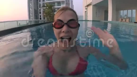 快乐开朗的年轻女子在游泳池的红色游泳套房里挥动着一只手操作摄像机视频的预览图