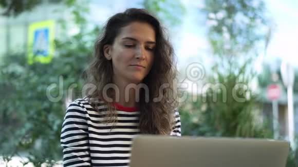 漂亮的年轻卷发深色头发在外面用笔记本电脑工作视频的预览图