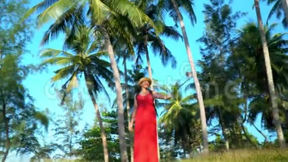 那个穿红色衣服的女人在岛上散步戴着草帽和自拍棒的女人女人拍自拍视频的预览图