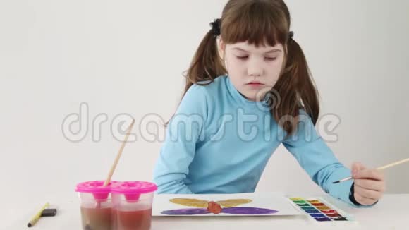 微笑美丽的女孩在桌子上画水彩蝶视频的预览图