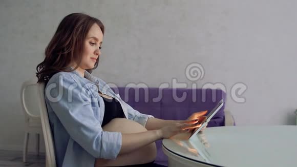 幸福的孕妇坐在玻璃餐桌旁喝咖啡用平板电脑从事商业活动视频的预览图