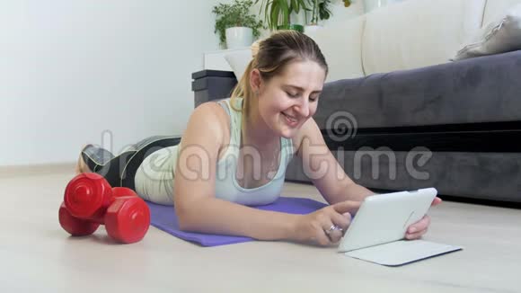 4k视频年轻运动女性在训练期间躺在健身垫上使用数码平板电脑视频的预览图