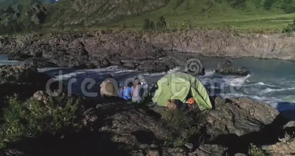 空中飞行一家带孩子的旅行者坐在帐篷附近欣赏山河和山脉视频的预览图