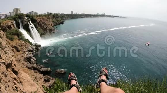 坐在悬崖上的人的腿和欣赏安塔利亚瀑布的图片视频的预览图