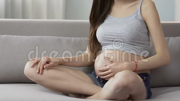 年轻的孕妇在沙发上做怀孕瑜伽身体活动健康视频的预览图