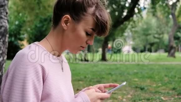 夏天公园里一位轻松的年轻女士在手机上读短信的肖像粉红色的漂亮少女视频的预览图